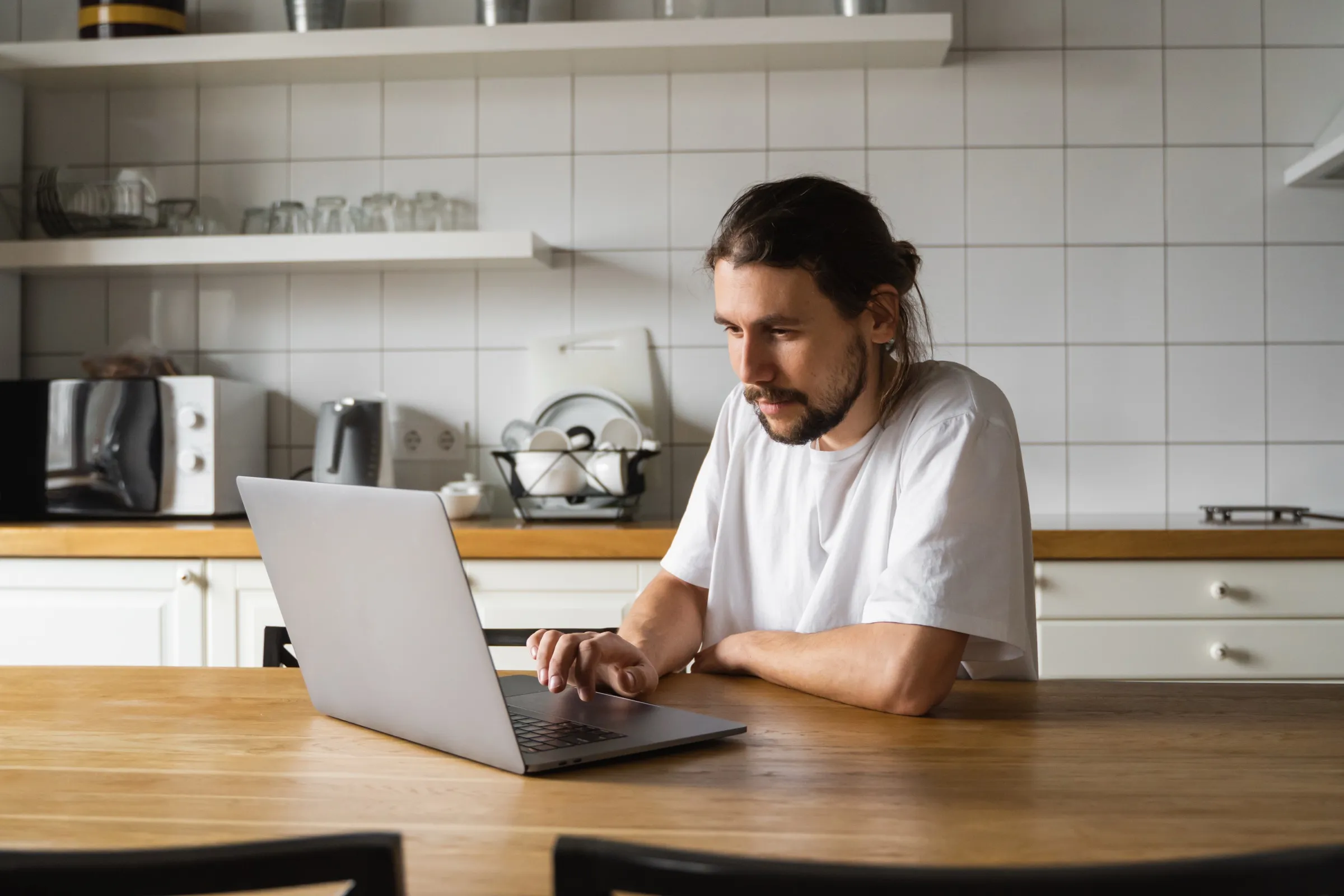 Someone working on a laptop at a kitchen table.