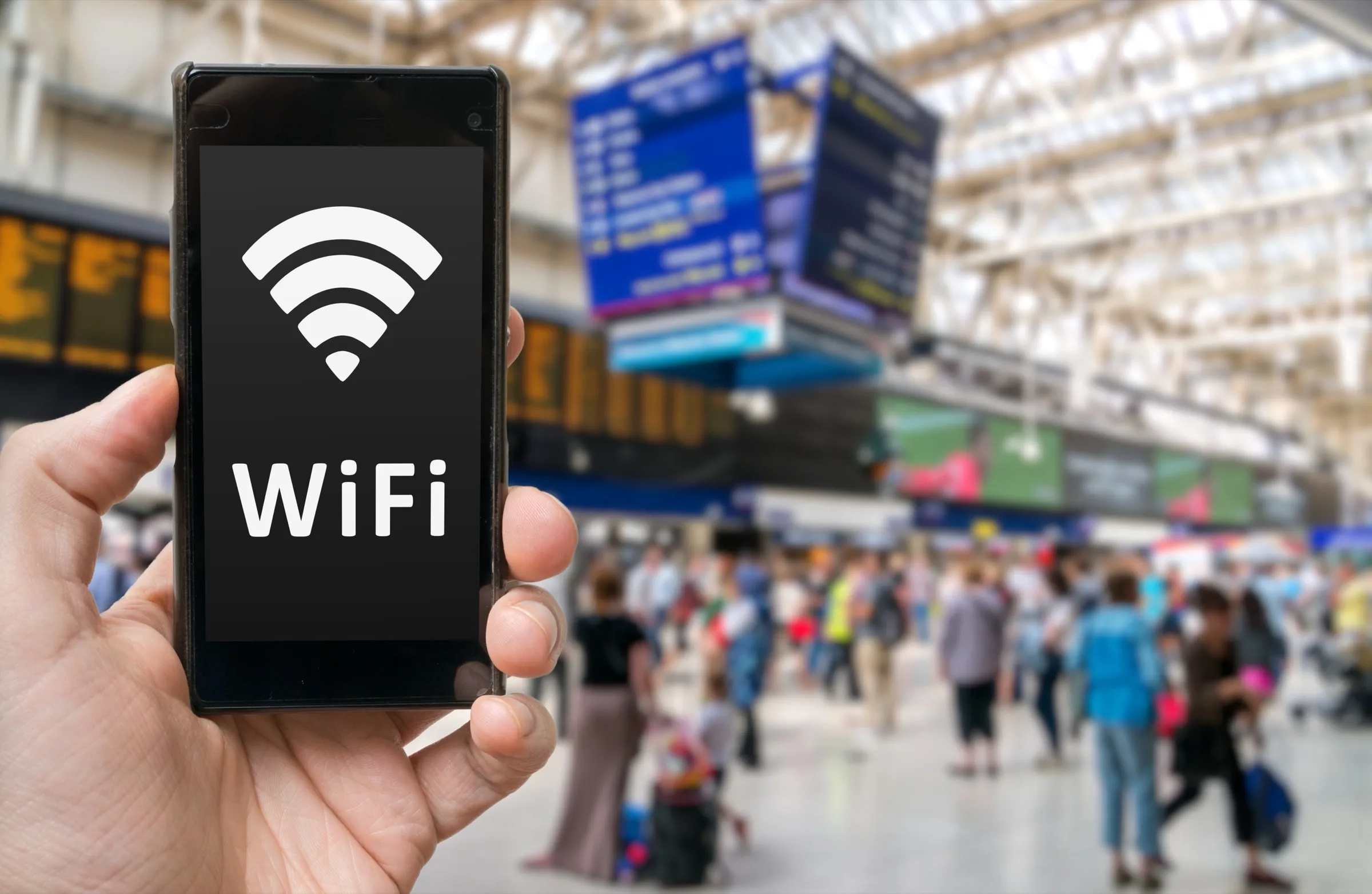 A hand holding a phone in a busy station concourse.